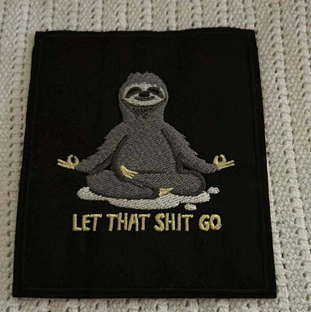 Black patch with embroidered meditating sloth and "LET THAT SHIT GO" text in beige