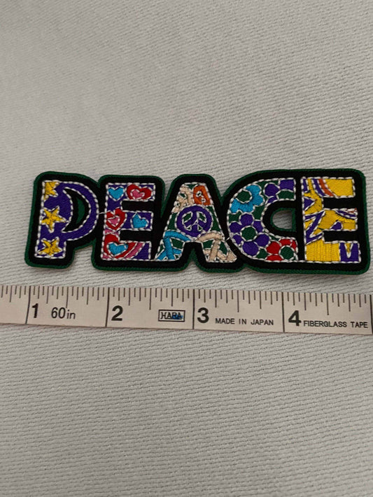 Colorful PEACE multicolored patch with floral and peace symbol designs placed above a measuring tape.