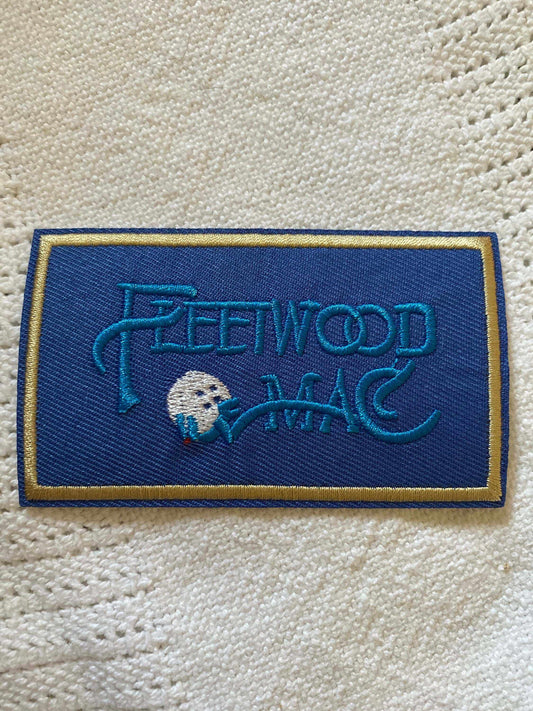 Blue embroidered Fleetwood Mac logo patch on white knitted fabric background