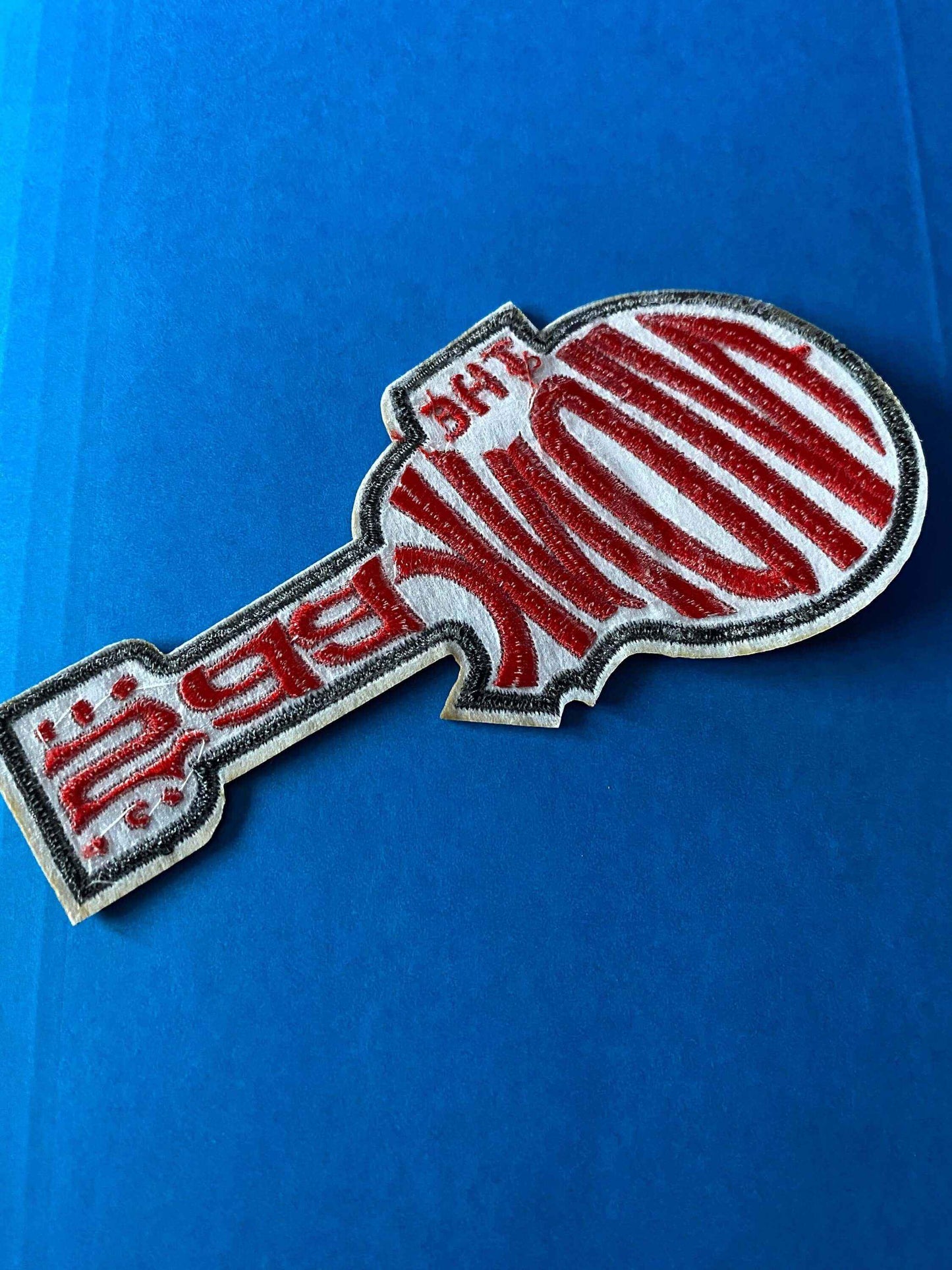 Embroidered Monkees logo patch shaped like a guitar with red and white stitching on a blue background